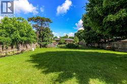 Expansive backyard featuring a lush green lawn, mature trees providing natural screening, and perimeter wood fencing - 