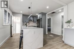 Modern kitchen featuring light gray cabinetry, stainless steel appliances, a white waterfall island with seating, and wood-finish flooring - 