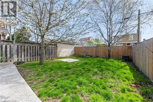 Expansive backyard with a concrete pathway, a central grass lawn, mature trees, and privacy fencing - 22 Cope Street, Hamilton, ON 