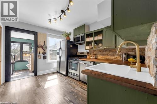 Kitchen featuring wood-finish flooring, olive green cabinetry, wooden countertops, a white undermount sink with a brass-finish faucet, and a brick-finish backsplash - 22 Cope Street, Hamilton, ON 