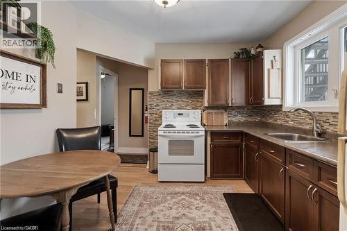 Kitchen featuring wood-finish flooring, dark wood cabinetry, a mosaic tile backsplash, and a stainless steel sink - 2 Mill Street E, York, ON 