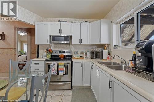 Kitchen featuring white cabinetry with dark hardware, stainless steel appliances, a double basin sink, and an exterior window - 2 Mill Street E, York, ON 