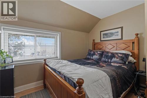 Bedroom featuring wood-finish flooring, a pitched ceiling, and a large window with white blinds - 2 Mill Street E, York, ON 