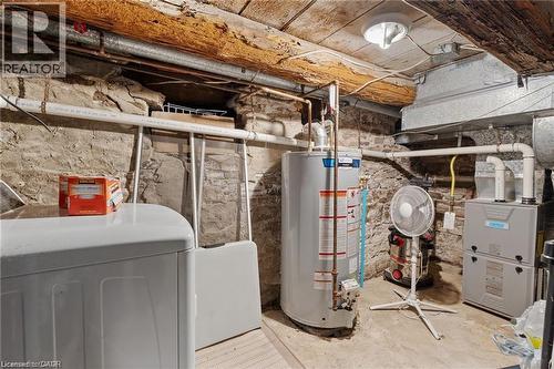 Basement utility area featuring exposed stone foundation walls, wood beam ceiling, and concrete flooring - 2 Mill Street E, York, ON 