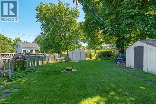 Expansive grassy backyard featuring two storage sheds, mature trees, and a wooden privacy fence - 2 Mill Street E, York, ON 