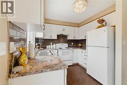 Kitchen featuring white cabinetry, a dual-basin stainless steel sink, and white appliances - 