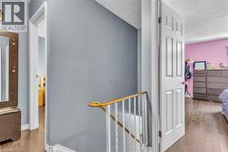 Upper landing featuring wood-finish flooring, a white railing with a brass-finish handrail, and a built-in wall mirror with hooks - 