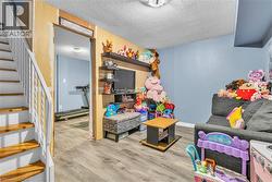 Wood-finish flooring throughout, featuring a staircase with white risers and handrails, an open doorway, and a ceiling-mounted light fixture - 