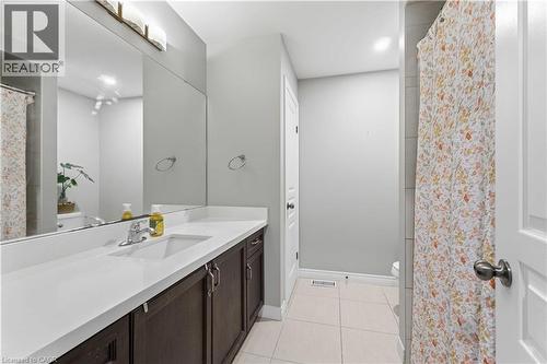 Bathroom featuring a dark wood-finish vanity with an integrated white sink, expansive mirror, and a three-light vanity fixture - 212 Chartwell Circle, Hamilton, ON 