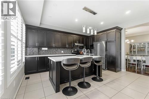 Modern kitchen featuring dark cabinetry, stainless steel appliances, a center island with seating, a mosaic tile backsplash, and plantation shutters - 212 Chartwell Circle, Hamilton, ON 