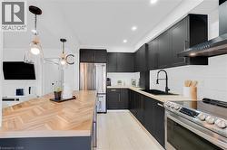 Modern kitchen featuring matte black cabinetry, light wood-finish countertops, stainless steel appliances, and a wood-finish herringbone island - 