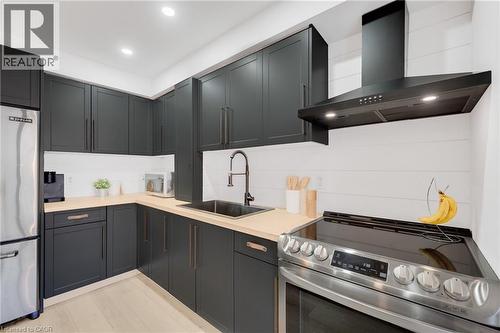 Modern kitchen featuring dark cabinetry with brushed bronze hardware, light wood-finish countertops, stainless steel appliances, and a shiplap backsplash - 5275 Banting Court, Burlington, ON 