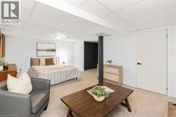 Carpeted lower-level room featuring a drop ceiling, white walls, and a five-panel interior door with matte black hardware - 