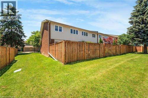 Expansive green lawn parcel framed by a wooden privacy fence, featuring a two-story residence with brick and siding exterior, multiple windows, and mature trees - 5275 Banting Court, Burlington, ON 