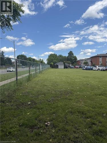 Expansive grassy area featuring a chain link fence and a clear blue sky with white clouds - 26 Carnaby Crescent, Kitchener, ON 