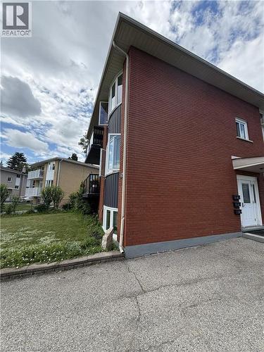 Brick exterior featuring a white entry door, multiple windows, a dark grey siding accent, and a paved parking area - 26 Carnaby Crescent, Kitchener, ON 
