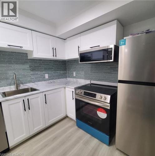 Contemporary kitchen featuring white cabinetry, a glass tile backsplash, and wood-finish flooring - 59 Highgate Road Unit# 2, Kitchener, ON 
