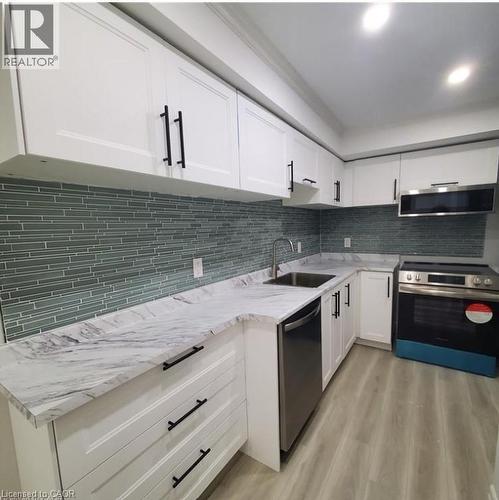 Modern kitchen featuring white cabinetry with black hardware, a light-toned marble-effect countertop, and a blue-green linear mosaic tile backsplash - 59 Highgate Road Unit# 2, Kitchener, ON 