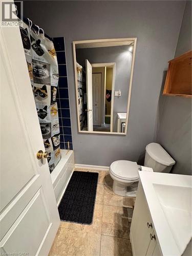 Bathroom featuring a white bathtub, blue tiled shower surround, framed wall mirror, white toilet, and a vanity with an integrated sink - 227 Fergus Avenue, Kitchener, ON 