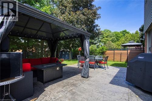 Expansive stamped concrete patio featuring a permanent gazebo with lighting, a privacy fence, and mature trees - 5 Shetland Drive, Waterdown, ON 