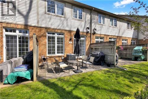 Patio area featuring brick and siding exterior, a sliding glass door, and multiple windows with white blinds - 120 Beddoe Drive Unit# 6, Hamilton, ON 