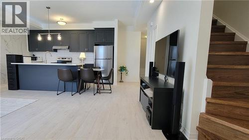 Open-concept living space featuring light wood-finish flooring, a kitchen with dark cabinetry and stainless steel appliances, a white subway tile backsplash, and a breakfast bar island - 142 Foamflower Place Unit# 12, Waterloo, ON - Indoor Photo Showing Kitchen With Upgraded Kitchen