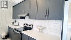 Contemporary kitchen featuring shaker-style cabinetry, a stainless steel range hood, white subway tile backsplash, and light-toned countertops - 