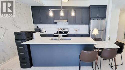 Contemporary kitchen featuring a spacious island with a built-in sink, dark cabinetry, stainless steel appliances, white subway tile backsplash, and light wood-finish flooring - 142 Foamflower Place Unit# 12, Waterloo, ON - Indoor Photo Showing Kitchen With Double Sink With Upgraded Kitchen