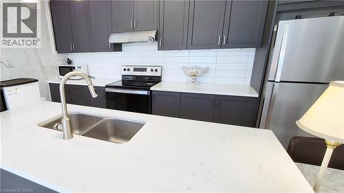 Contemporary kitchen featuring a dual-basin stainless steel sink with a high-arc faucet, white countertops, dark cabinetry, and a white subway tile backsplash - 142 Foamflower Place Unit# 12, Waterloo, ON - Indoor Photo Showing Kitchen With Double Sink With Upgraded Kitchen