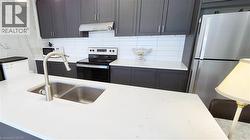 Contemporary kitchen featuring a dual-basin stainless steel sink with a high-arc faucet, white countertops, dark cabinetry, and a white subway tile backsplash - 
