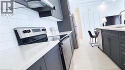 Modern kitchen featuring dark grey cabinetry, light countertops, stainless steel appliances, and a white subway tile backsplash - 