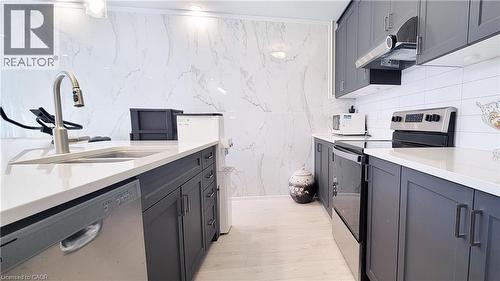 Modern kitchen featuring dark cabinetry, light countertops, stainless steel appliances, a tile backsplash, and light wood-finish flooring - 142 Foamflower Place Unit# 12, Waterloo, ON - Indoor Photo Showing Kitchen With Double Sink