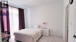 Room featuring light wood-finish flooring, white walls, and a window with sheer and blackout curtains - 
