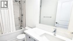 Bathroom featuring a white bathtub with a tile surround, a built-in toilet, a single vanity with a white countertop, an undermount sink, and a chrome faucet - 