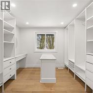 Bright, organized space featuring extensive built-in white shelving, recessed lighting, and wood-finish flooring - 