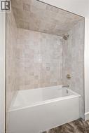Bathtub and shower combination featuring neutral square wall tiles, a white porcelain tub, and brushed nickel fixtures - 