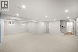 Spacious finished lower level featuring recessed lighting, light-toned carpeting, egress windows, and a staircase with a black handrail - 