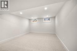 Spacious room featuring light-toned carpeting, neutral wall paint, recessed ceiling lighting, and two egress windows - 