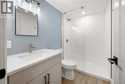 Full bathroom featuring a glass-enclosed shower, single vanity with integrated sink, wood-finish flooring, and contemporary light fixtures - 