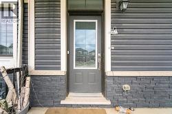 Entry door with upper glass panel, dark gray siding, stone-finish foundation, light-colored trim, and an exterior light fixture - 