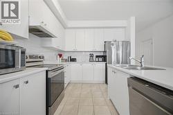 Contemporary kitchen featuring white cabinetry, stainless steel appliances, a double basin sink, light-toned tile flooring, and a subway tile backsplash - 