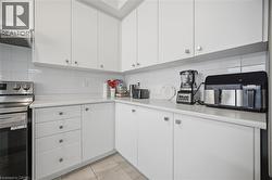 Contemporary kitchen featuring white cabinetry, a white subway tile backsplash, light-toned countertops, stainless steel appliances, and tile flooring - 
