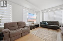 Living area featuring light wood-finish flooring, white walls, and multiple windows with horizontal blinds - 