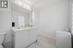 Bathroom featuring a white vanity with integrated sink, a large wall-mounted mirror with overhead lighting, and light-toned floor tiles - 