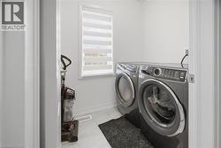 Dedicated laundry area featuring a front-loading washer and dryer, a window with horizontal blinds, and light-toned flooring - 