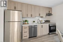 Contemporary kitchen featuring light wood-finish cabinetry with black hardware, stainless steel appliances, white countertops, and wood-finish flooring - 