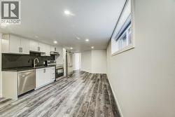 Contemporary kitchen featuring white cabinetry, dark countertops, a stainless steel appliance suite, and wood-finish flooring - 