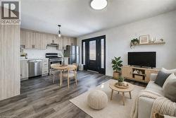 Open-concept living area featuring wood-finish flooring, a contemporary kitchen with stainless steel appliances, and light-toned cabinetry - 