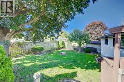 Expansive green lawn with mature shade trees, bordered by a wooden privacy fence - 