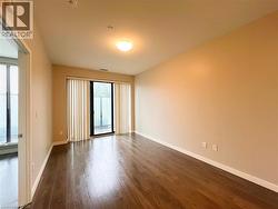 Spacious room featuring wood-finish flooring, neutral-toned walls, and a sliding glass door with vertical blinds - 